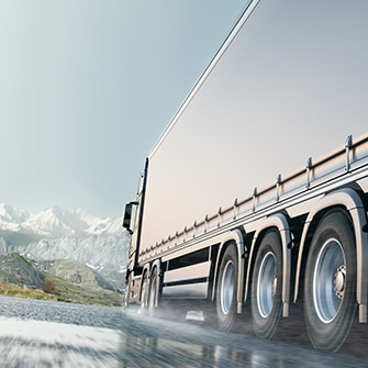 A truck driving down the road with mountains in the background.