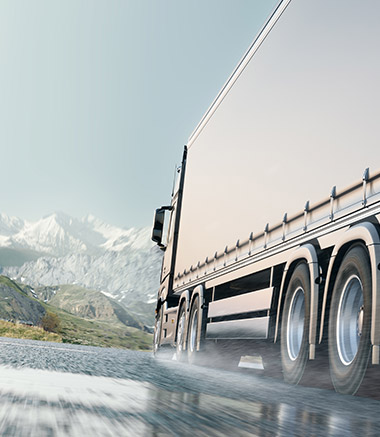 A truck driving down the road with mountains in the background.